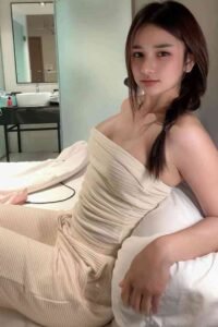 Woman in cream-colored outfit sitting on a bed.