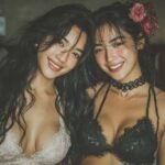 Two young women smiling, wearing lingerie, with one holding a flower in her hair.