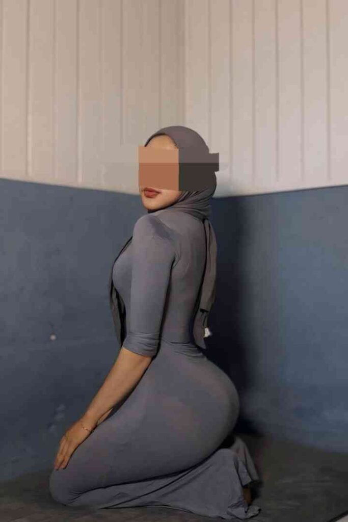 Malay woman in grey dress and hijab kneeling, side view. Dila in KL.