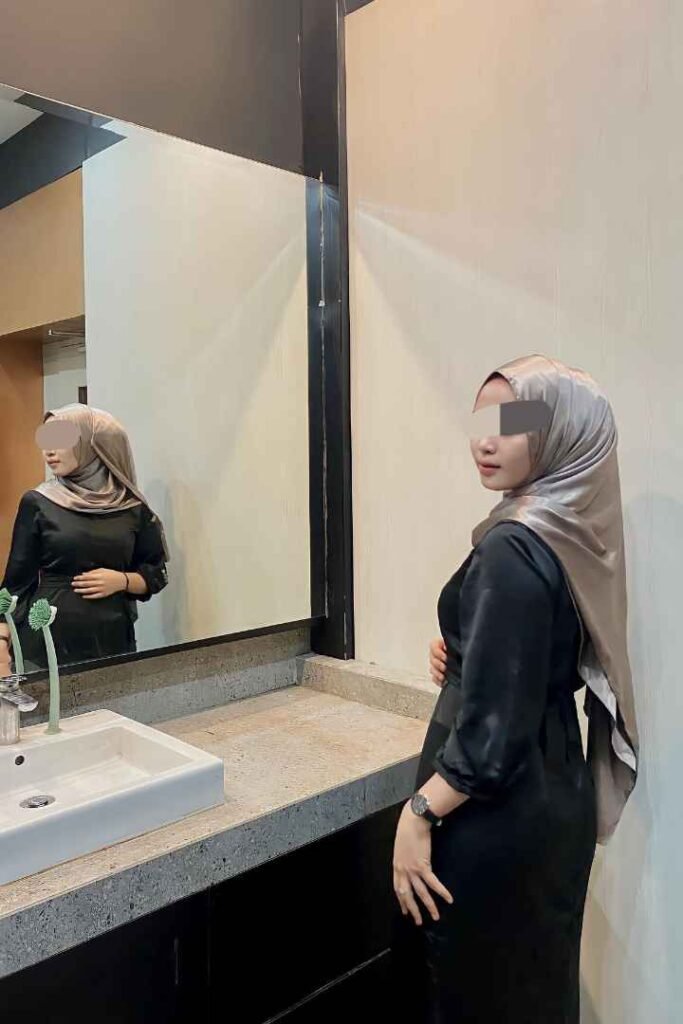 Malay woman in hijab and black dress, reflected in a mirror.