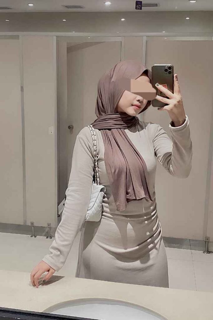 Malay woman in hijab taking a mirror selfie in a bathroom.