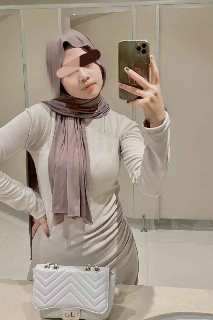 Woman in hijab taking a selfie with a white purse.